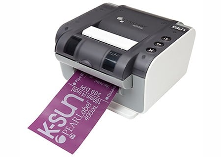 A desktop label printer dispensing a purple printed label.