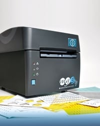 A black desktop printer with blue accents sits on a surface with papers and sticky notes nearby.