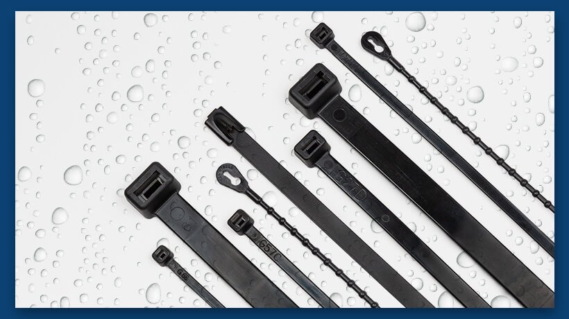 Six black cable ties of varying sizes arranged diagonally on a wet white surface.