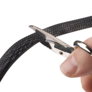 A person uses scissors to cut black braided cable sleeving.